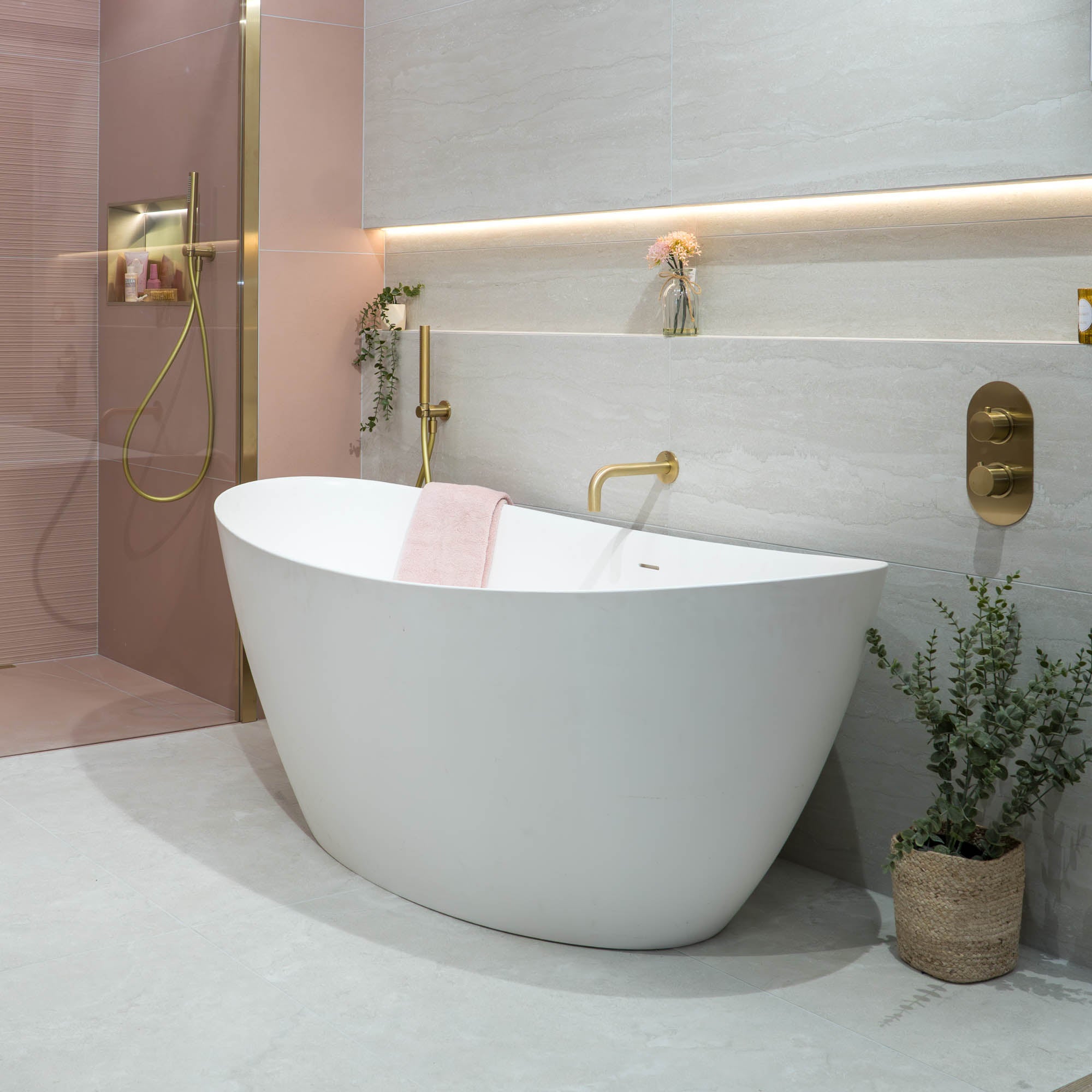 Modern bathroom with a freestanding white bathtub, gold fixtures, and a plant.