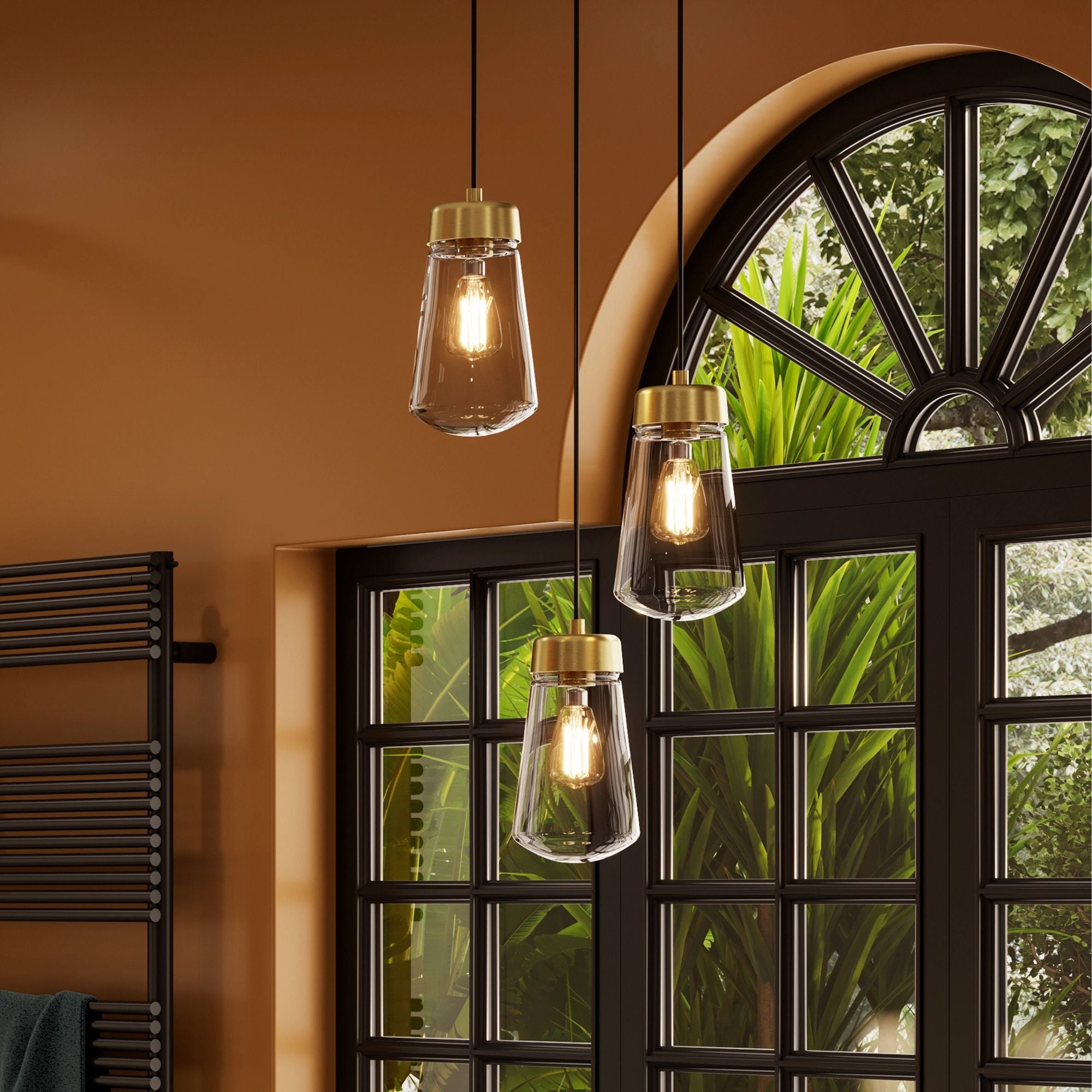Hib summit brushed brass finish three hanging pendant lights with glass shades in a room with a window and plant.