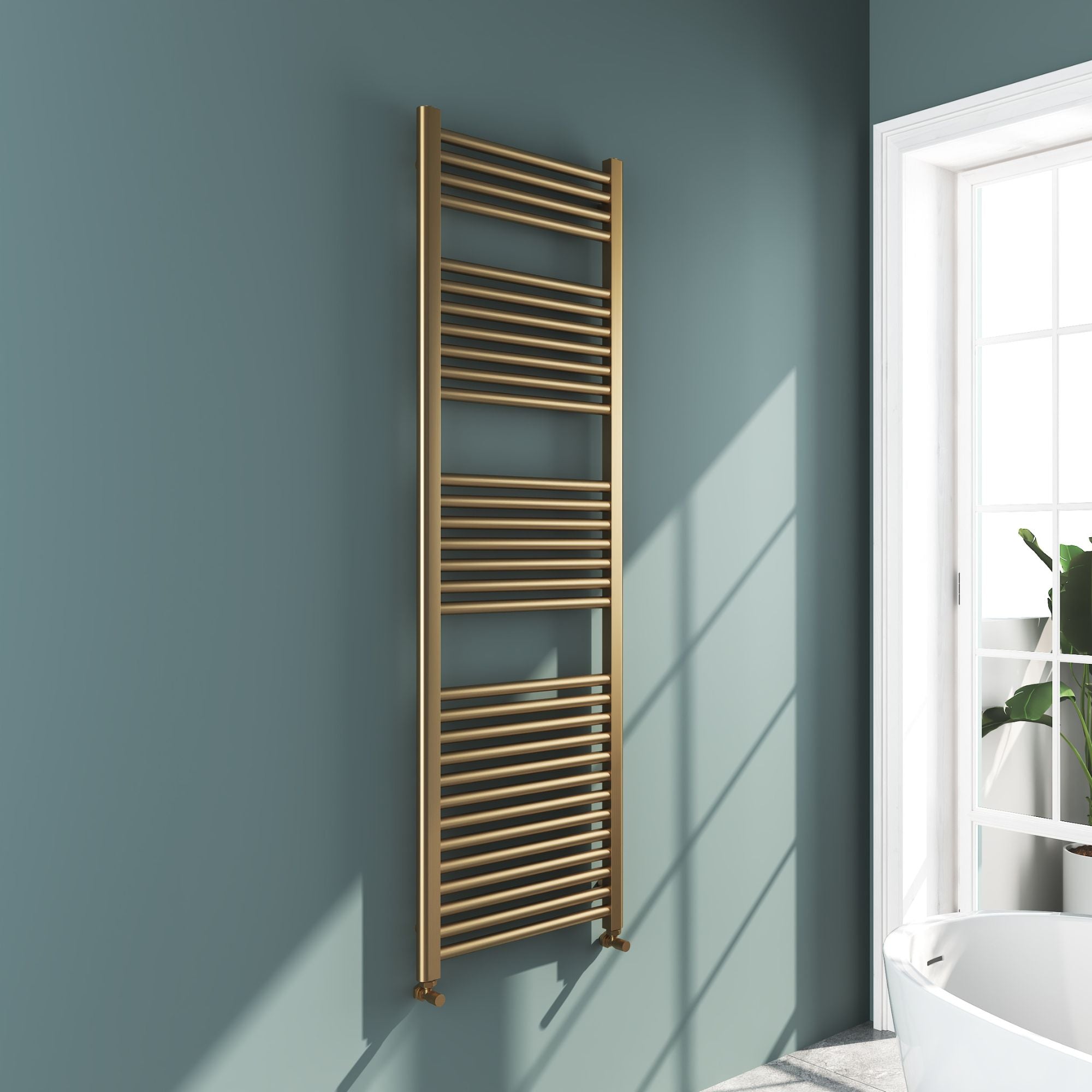 Soho brushed brass 1600x500mm towel radiator on a light blue wall with a window in the background deluxe bathrooms