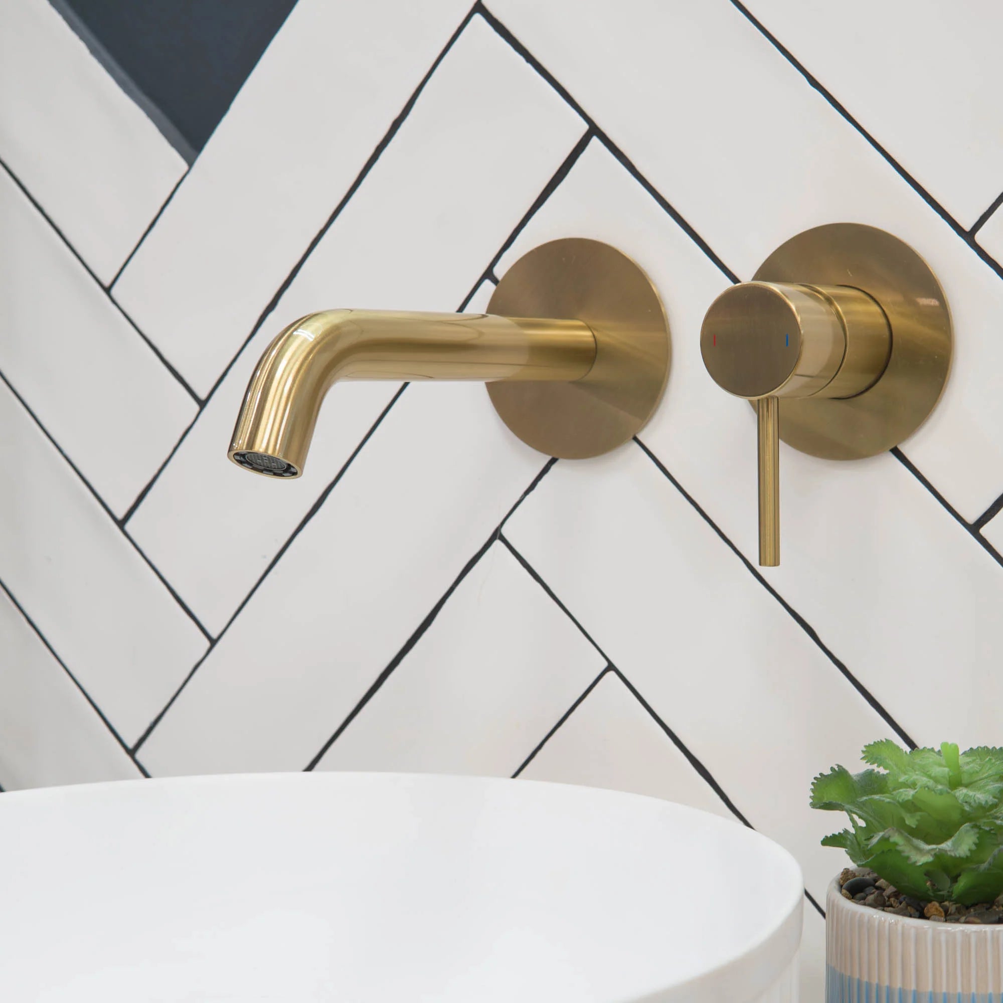 brushed brass bathroom faucet and handle set against a white tiled wall with a plant in the corner deluxe bathrooms.