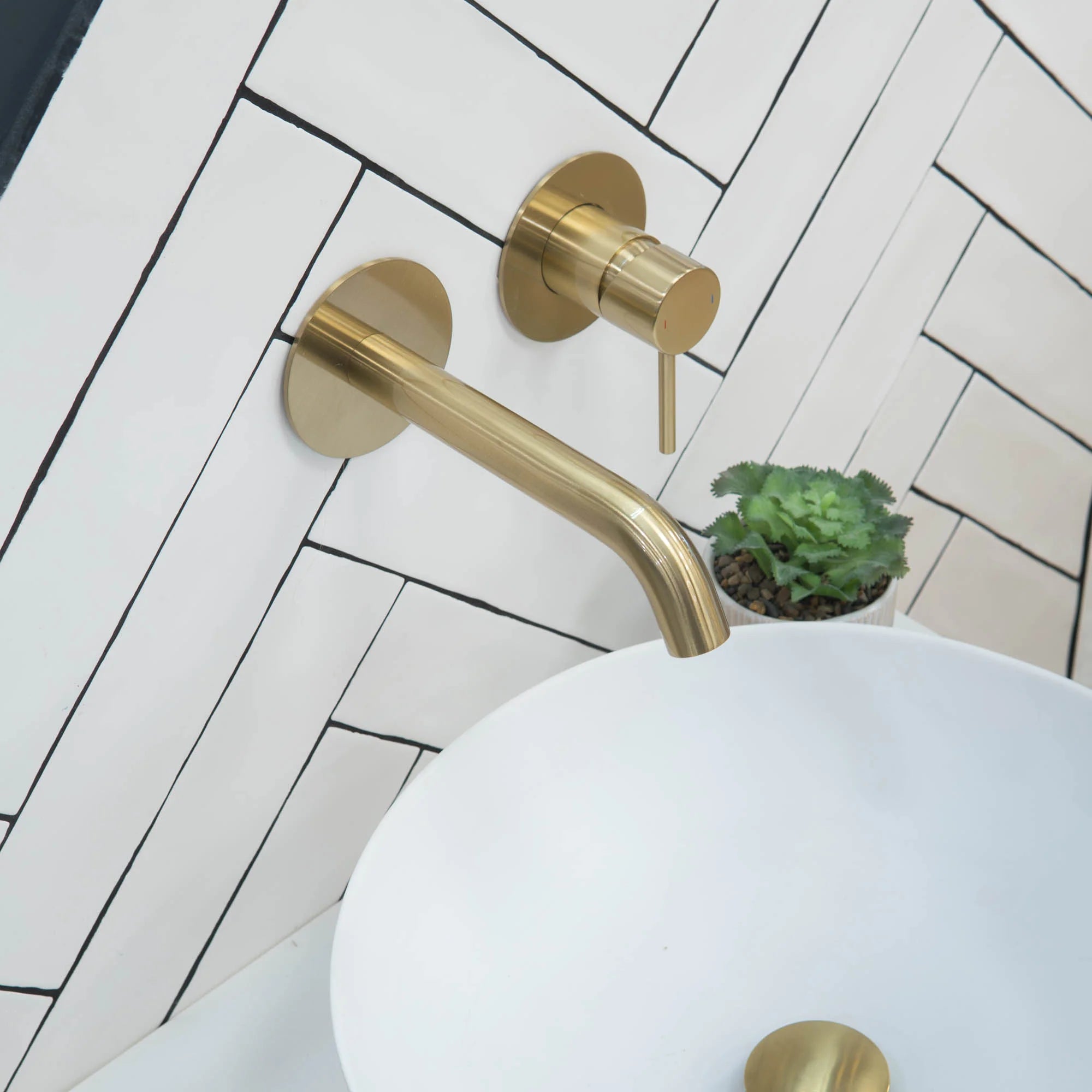 brushed brass bathroom faucet and handle set against a white tiled wall with a plant in the corner deluxe bathrooms