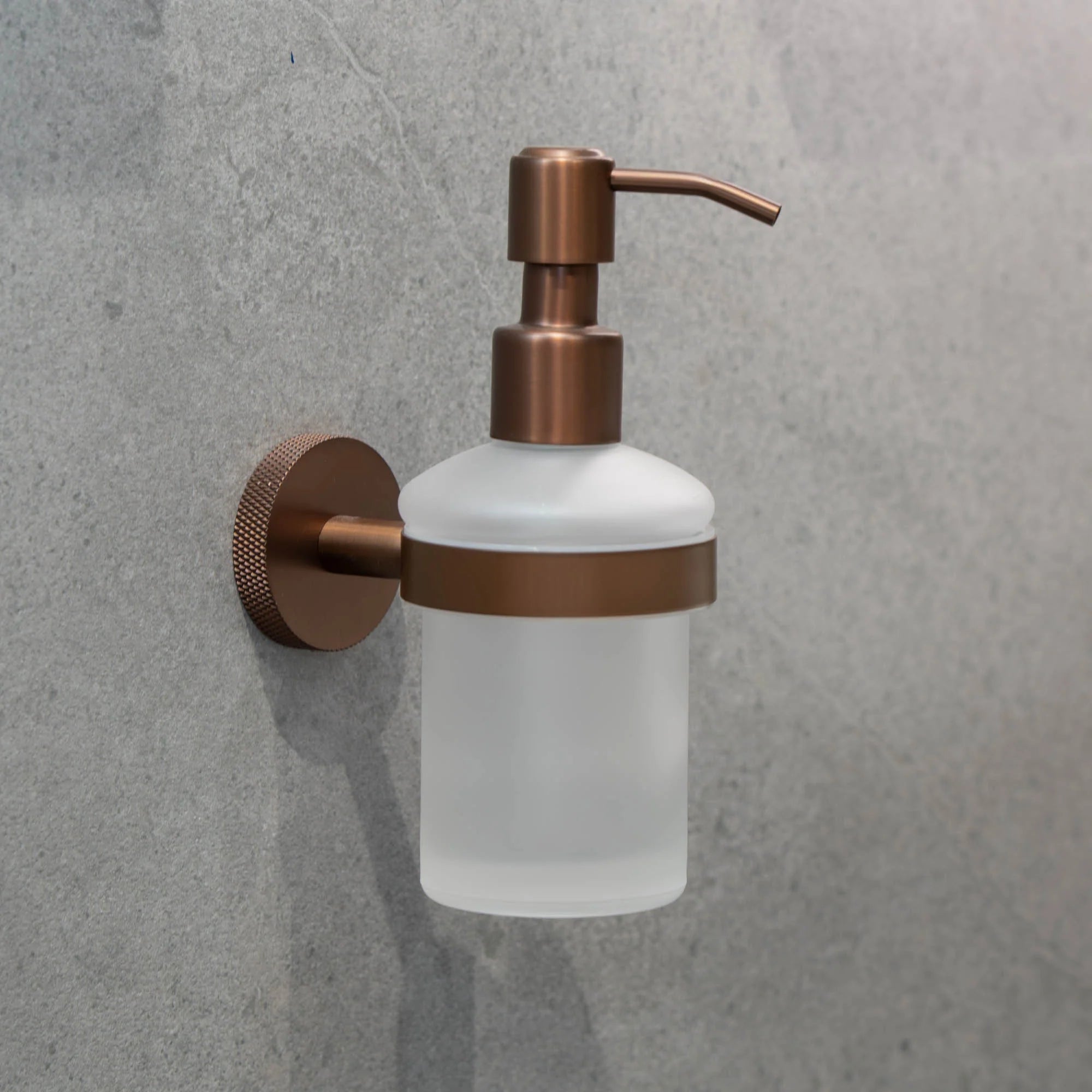 Wall-mounted portofino soap dispenser with bronze pump and frosted container on a grey wall deluxe bathrooms