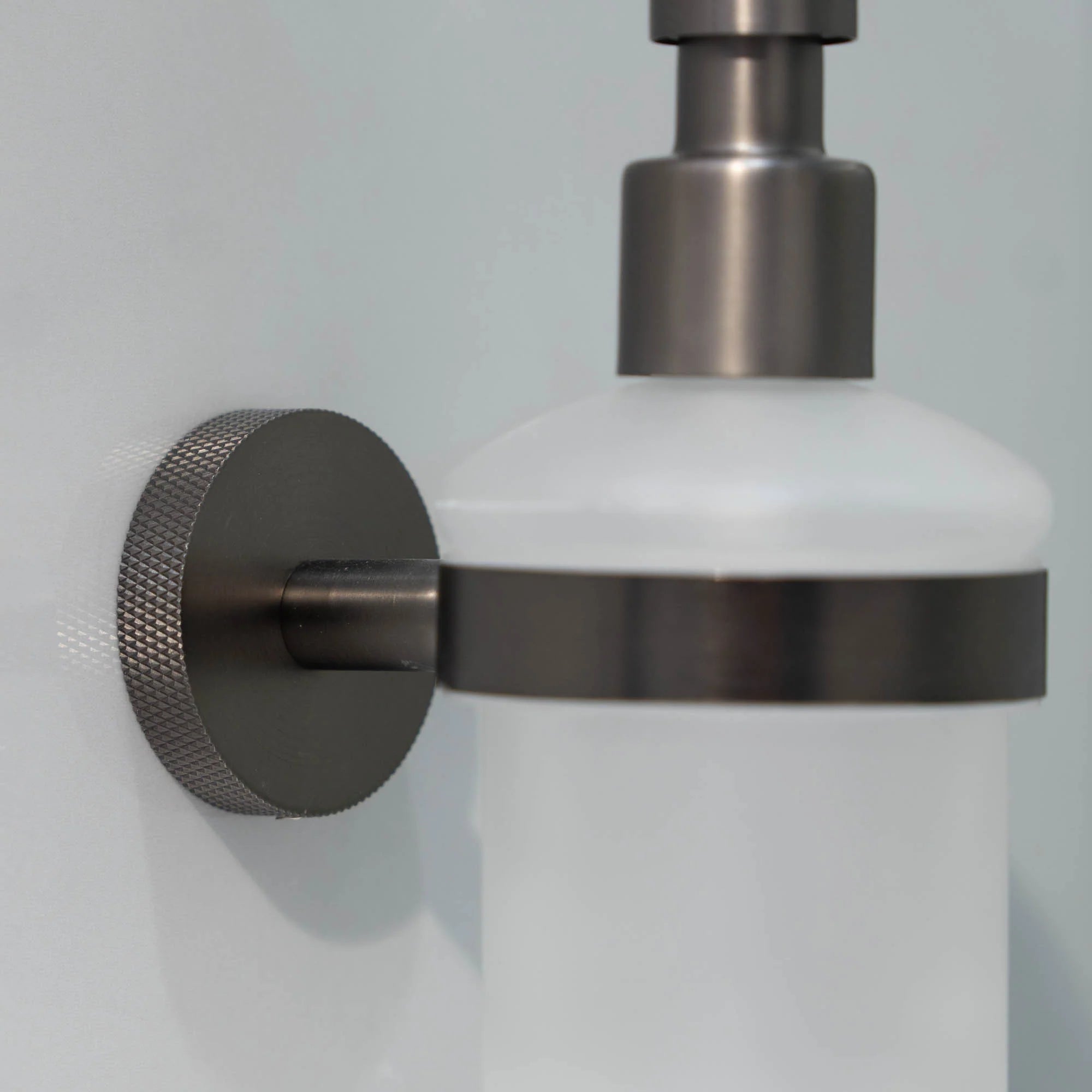 Wall-mounted portofino soap dispenser with gunmetal pump and frosted container on a grey wall deluxe bathrooms