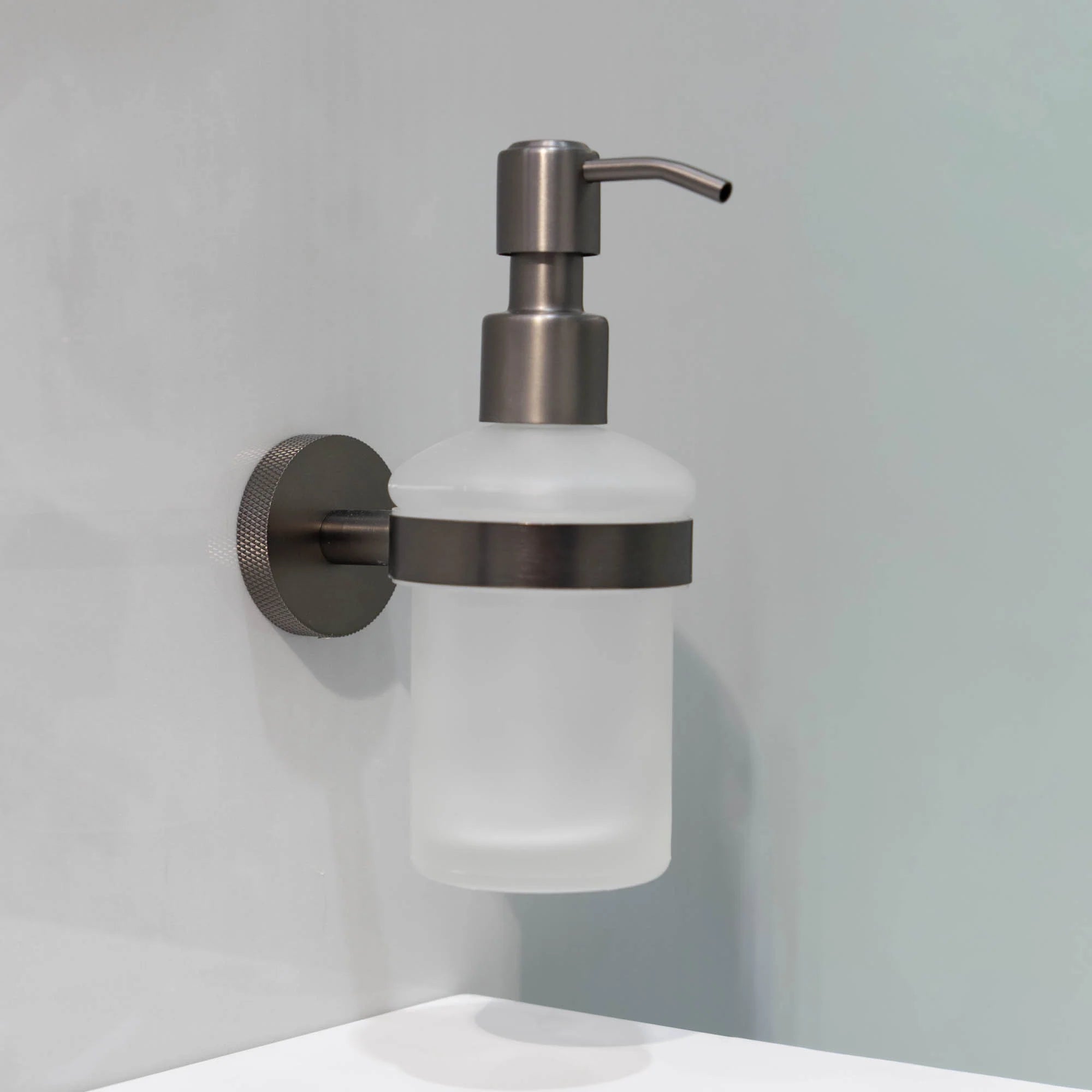 Wall-mounted portofino soap dispenser with gunmetal pump and frosted container on a grey wall deluxe bathrooms